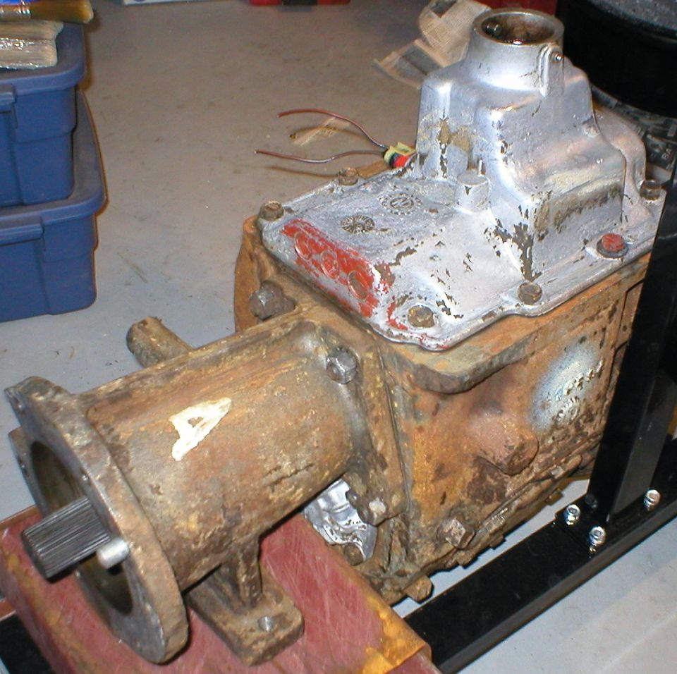 Rusty manual transmission with aluminum top cover on wood blocks in a garage