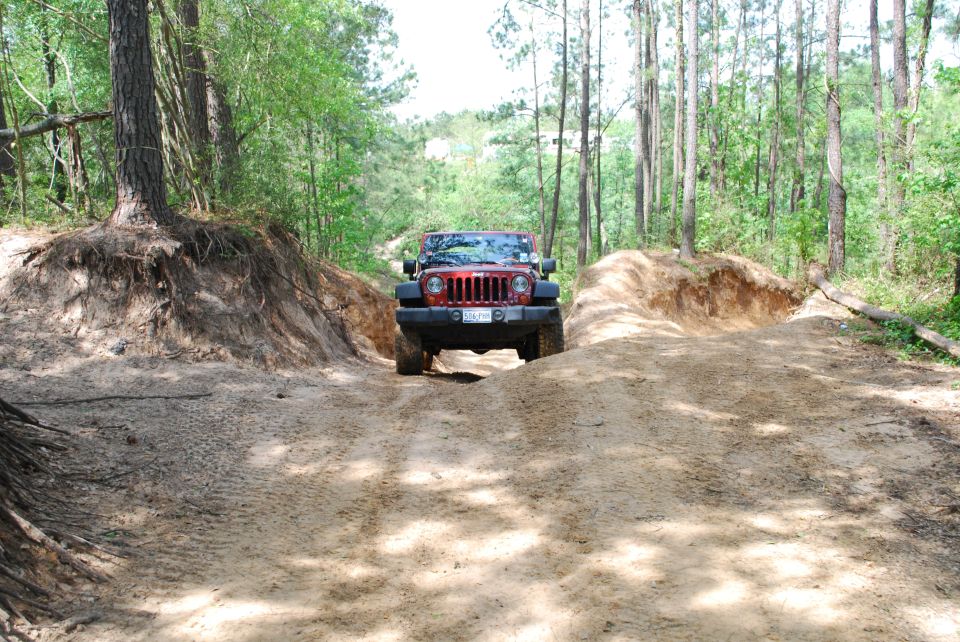 Red 2007 Jeep Wrangler driving on a sandy dirt track through a wooded area