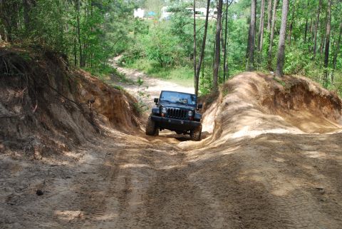 2008 Jeep Wrangler - A black Jeep Wrangler navigates a challenging off-road trail through a wooded area.