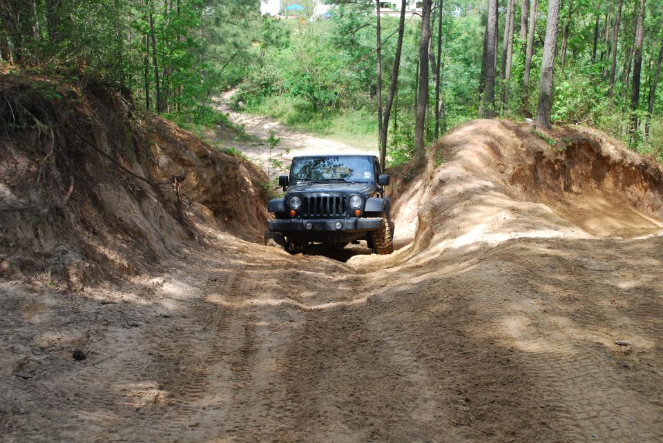 Black 2007 Jeep Wrangler driving on a sandy trail between dirt mounds