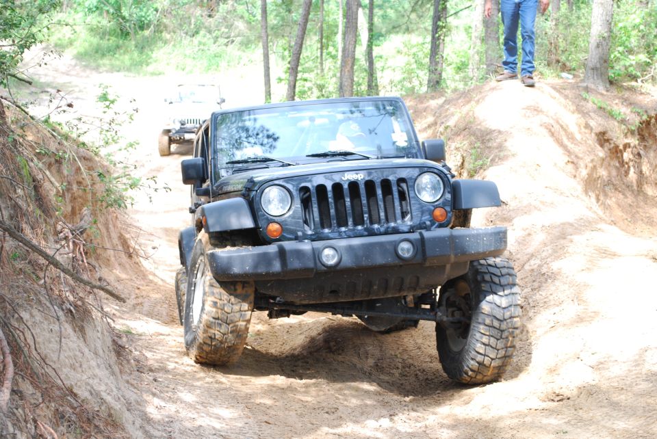 Black Jeep Wrangler with large tires driving on a dirt trail, front view