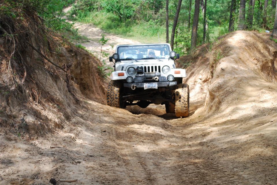 White Jeep Wrangler with winch on front bumper driving up a sandy hill, front view