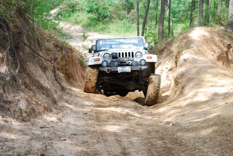 2008 Jeep Wrangler - A white lifted Jeep Wrangler TJ noses down a deep sand-and-clay rut in the woods, front axle articulating with one muddy 35-inch tire hangi…