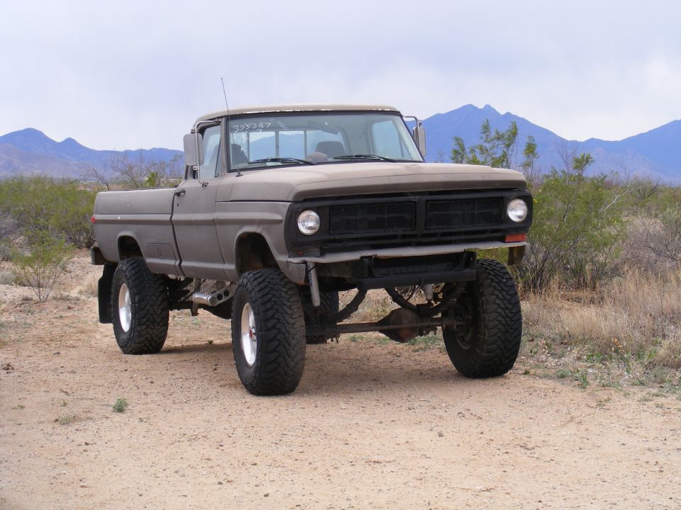 Gray lifted pickup truck with large tires, front view. Some text is visible on the windshield