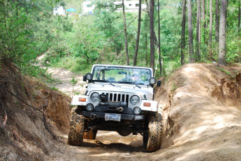 2008 Jeep Wrangler - A white 2008 Jeep Wrangler navigates a challenging dirt trail, its large tires kicking up dust.