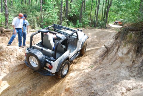 2008 Jeep Wrangler - White Jeep Wrangler navigating a sandy, wooded trail with another vehicle in the background.