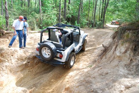 2008 Jeep Wrangler - Two people watch a white Jeep Wrangler navigate a challenging off-road trail in a wooded area.