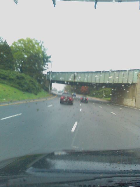 1996 Ford Bronco - Two cars are visible on a wet highway under a green overpass with trees on the side.