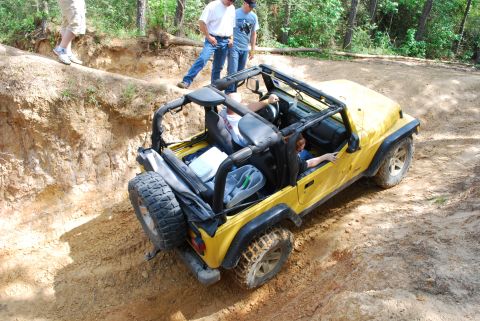 2008 Jeep Wrangler - Yellow 2008 Jeep Wrangler off-roading on a dirt trail with passengers.
