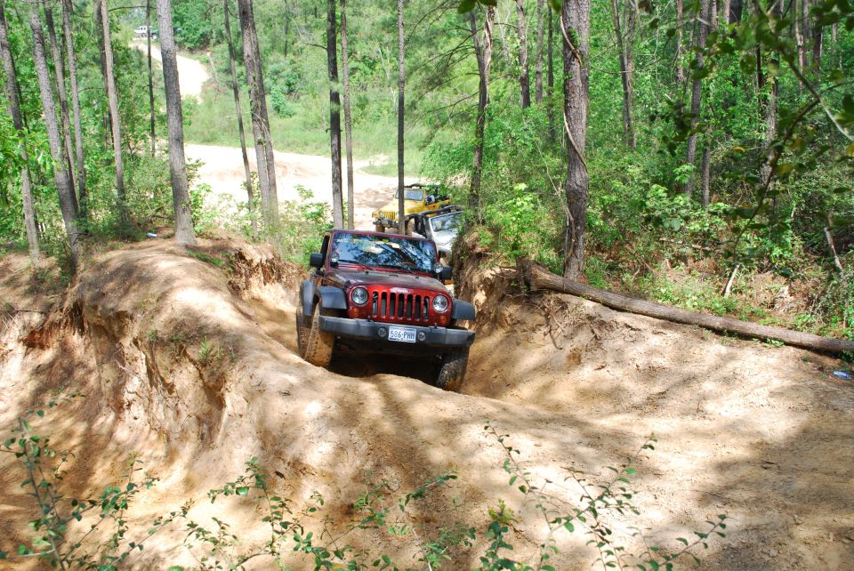 Red 2008 Jeep Wrangler on a dirt trail with other vehicles behind it