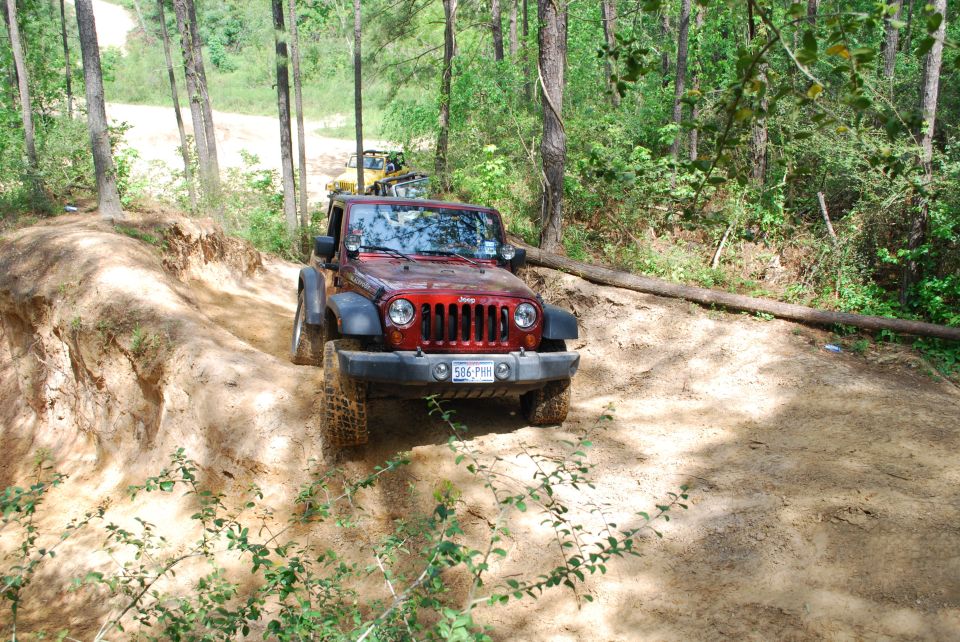 Red Jeep Wrangler on a dirt trail, front view. License plate 586 PHM. Another vehicle visible in the background