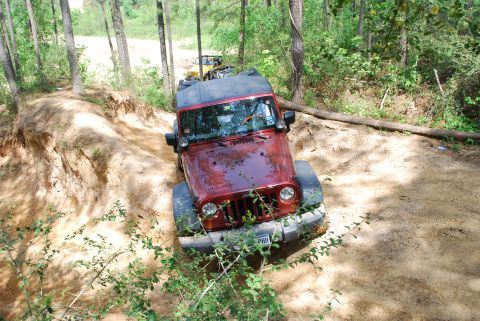 2008 Jeep Wrangler - A red Jeep Wrangler navigates a challenging dirt trail, with another vehicle following closely behind.