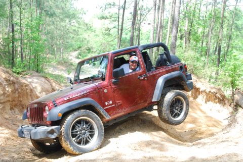 2008 Jeep Wrangler - Driver navigates a red 2008 Jeep Wrangler JK through an off-road trail with one wheel in the air.