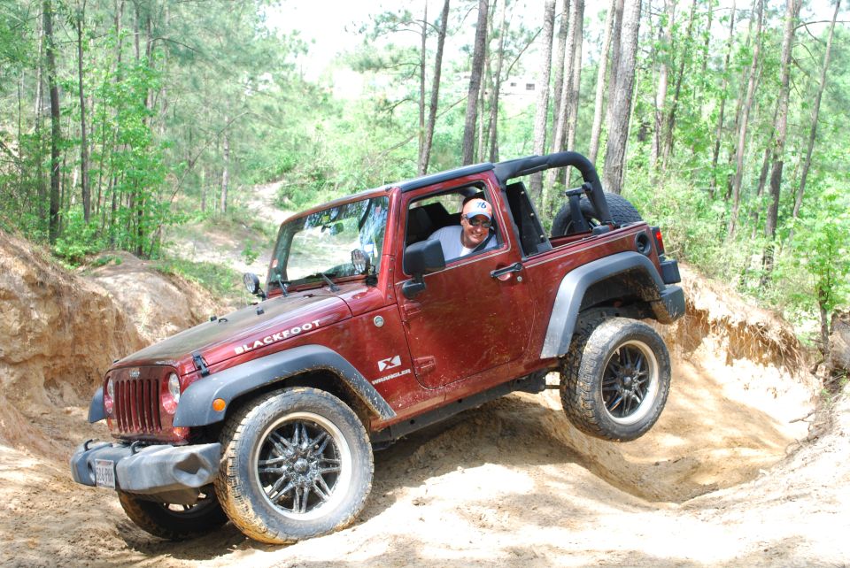 Red Jeep Wrangler with "BLACKFOOT" on the hood, driving on a dirt trail with one wheel off the ground