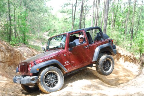 2008 Jeep Wrangler - A red Jeep Wrangler navigates an off-road trail with one wheel lifted.