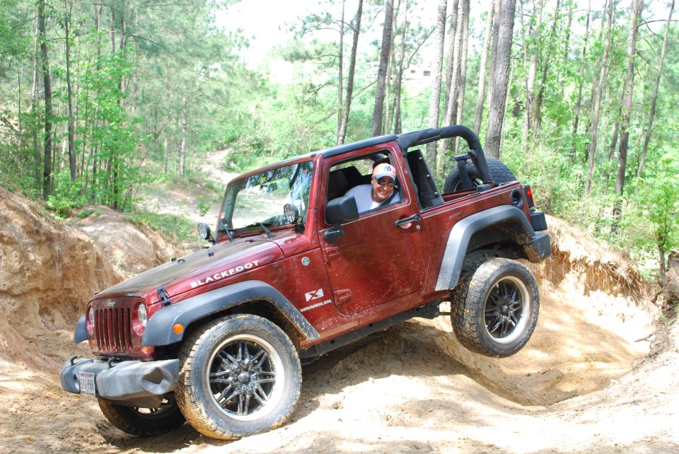 Red Jeep Wrangler with black aftermarket wheels driving on a dirt trail, driver visible