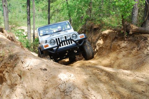2008 Jeep Wrangler - A white lifted Jeep Wrangler TJ with no top drops into a deep sandy trail rut in a pine forest, front axle flexed and steel tube front bump…