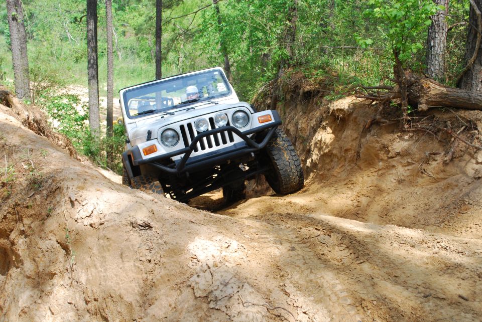 White topless Jeep Wrangler TJ with tube bumper crawling into a sandy forest rut