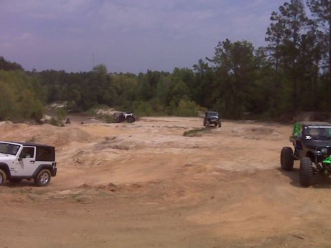 2008 Jeep Wrangler - Multiple off-road vehicles are gathered at a sandy park, with some driving and others parked.
