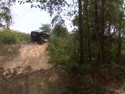 2008 Jeep Wrangler - A black Jeep Wrangler navigates an off-road trail, ascending a dusty incline amidst dense woodland.