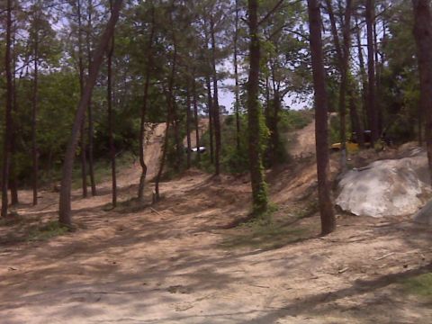 2008 Jeep Wrangler - A wooded off-road area with dirt mounds and trees, a distant white vehicle.