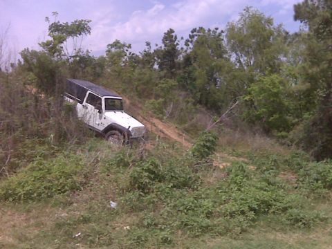 2008 Jeep Wrangler - A white Jeep Wrangler navigates a steep, overgrown dirt trail under a cloudy sky.