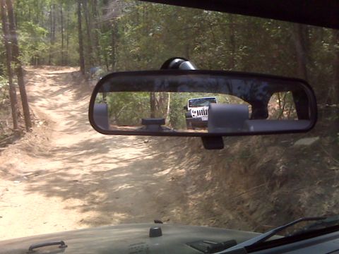 2008 Jeep Wrangler - A white Jeep Wrangler is visible in the rearview mirror on a wooded dirt road.