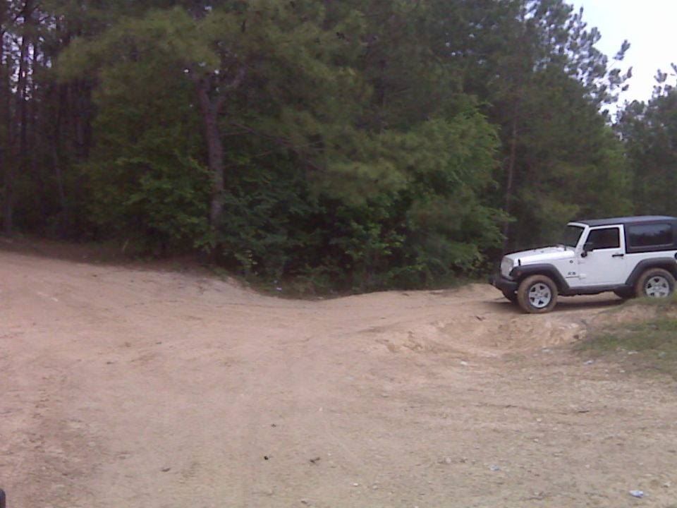 White Jeep Wrangler on a dirt road with trees in the background