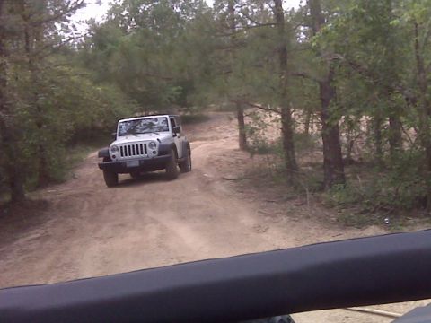 2008 Jeep Wrangler - A white Jeep Wrangler navigates a sandy track surrounded by trees, seen from the perspective of another vehicle.
