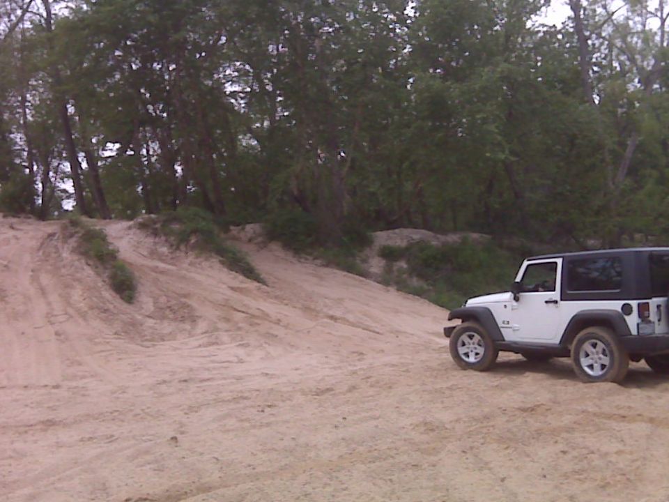 White 2007 Jeep Wrangler parked on a sandy hill with trees in the background