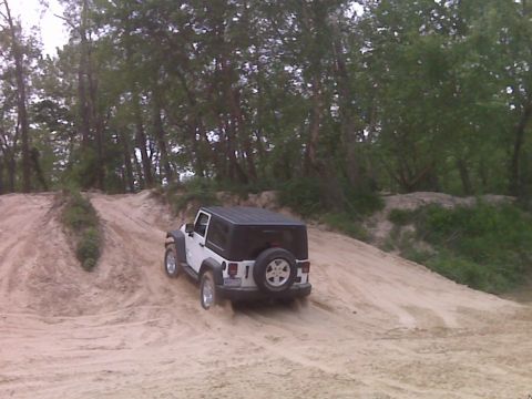2008 Jeep Wrangler - A white Jeep Wrangler navigates a sandy terrain, kicking up dust as it climbs.
