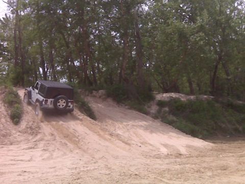 2008 Jeep Wrangler - A white Jeep Wrangler navigates a sandy incline with trees in the background.