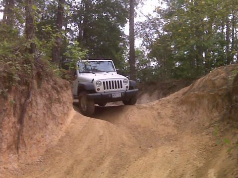2008 Jeep Wrangler - A white topless Jeep Wrangler JK crawls down a rutted clay trail cut between eroded dirt banks in a wooded area, viewed from the front with…