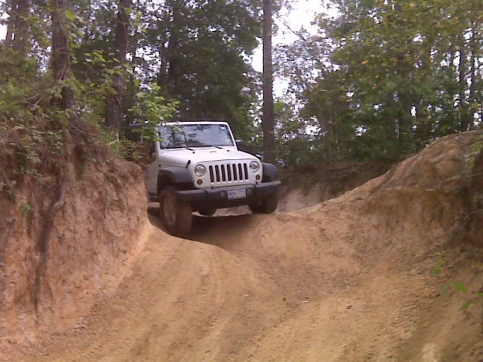 White topless Jeep Wrangler JK descending a rutted clay trail between dirt banks