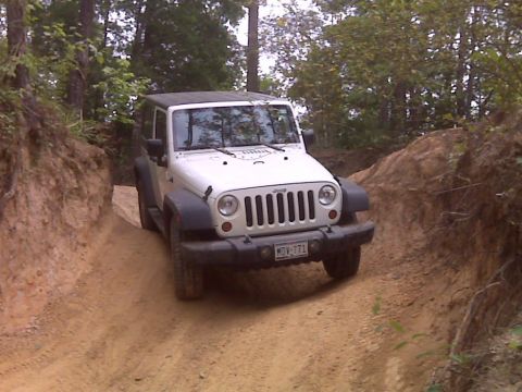 2008 Jeep Wrangler - A white Jeep Wrangler navigates a narrow dirt path surrounded by wooded terrain.