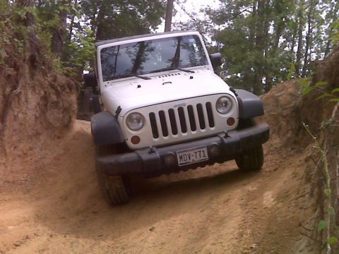 2008 Jeep Wrangler - A white Jeep Wrangler navigates a narrow dirt path through a wooded area.