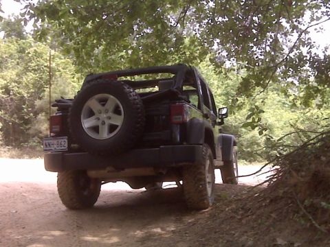 2008 Jeep Wrangler - A black 2008 Jeep Wrangler is seen from the rear on a dirt path surrounded by trees.