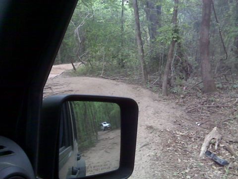 2008 Jeep Wrangler - Driving on a dirt path through a wooded area, with another vehicle visible in the side mirror.