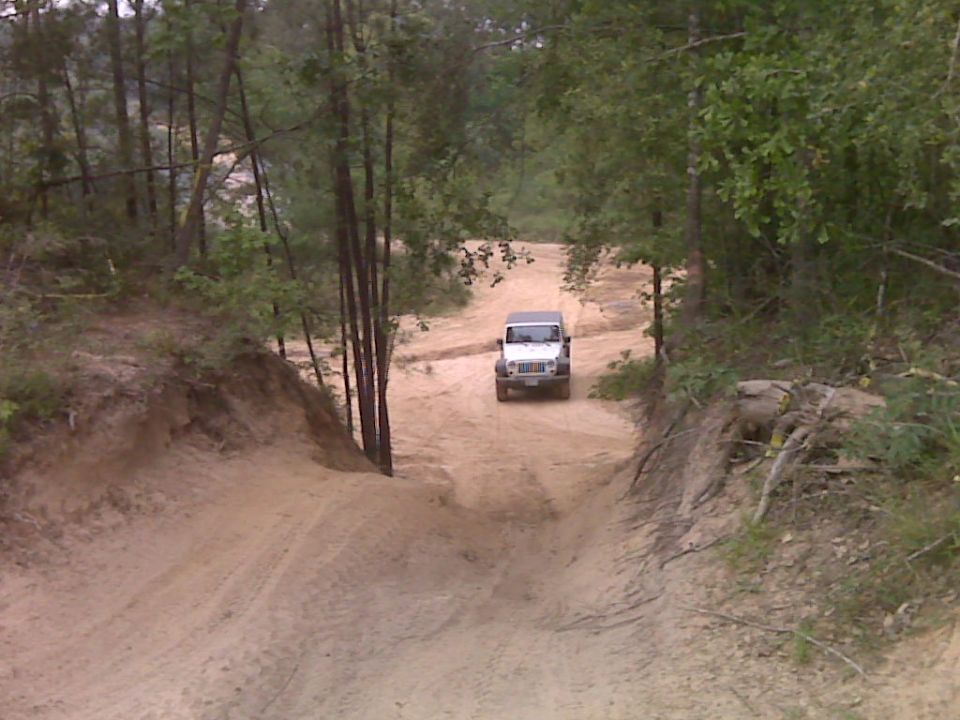 White Jeep Wrangler on a sandy trail, front view. The vehicle appears to be a JK generation