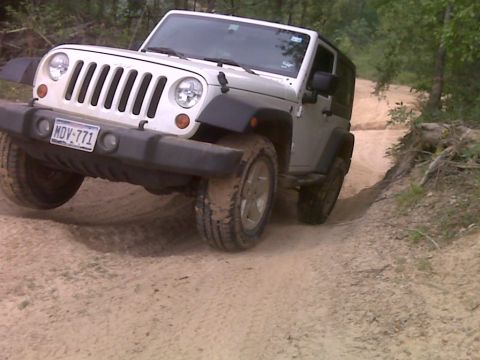 2008 Jeep Wrangler - A Jeep Wrangler navigates a muddy off-road trail surrounded by trees.