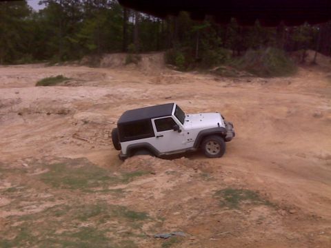 2008 Jeep Wrangler - White Jeep Wrangler navigating challenging dirt terrain, with one wheel partially submerged.