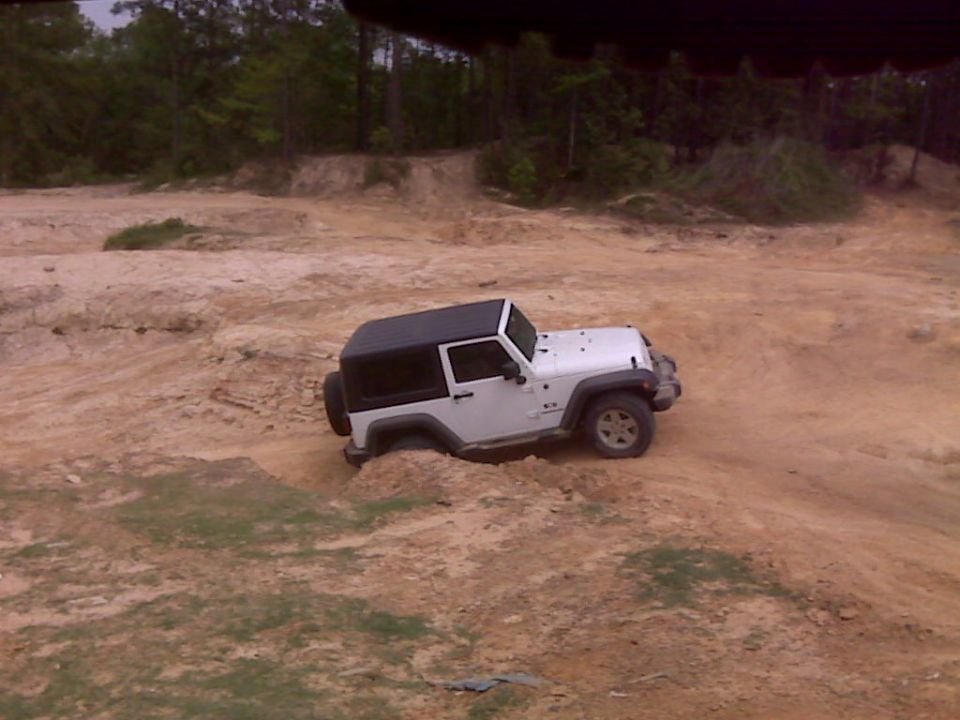 White Jeep Wrangler with black hardtop stuck in dirt during off-road excursion