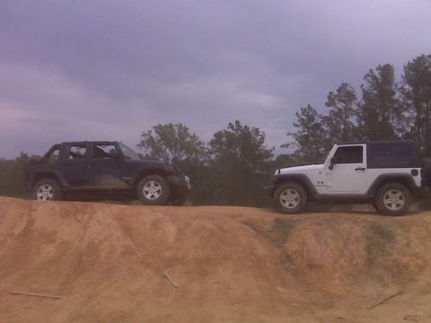 2008 Jeep Wrangler - Two Jeep Wranglers are positioned on a dirt hill under a cloudy sky.