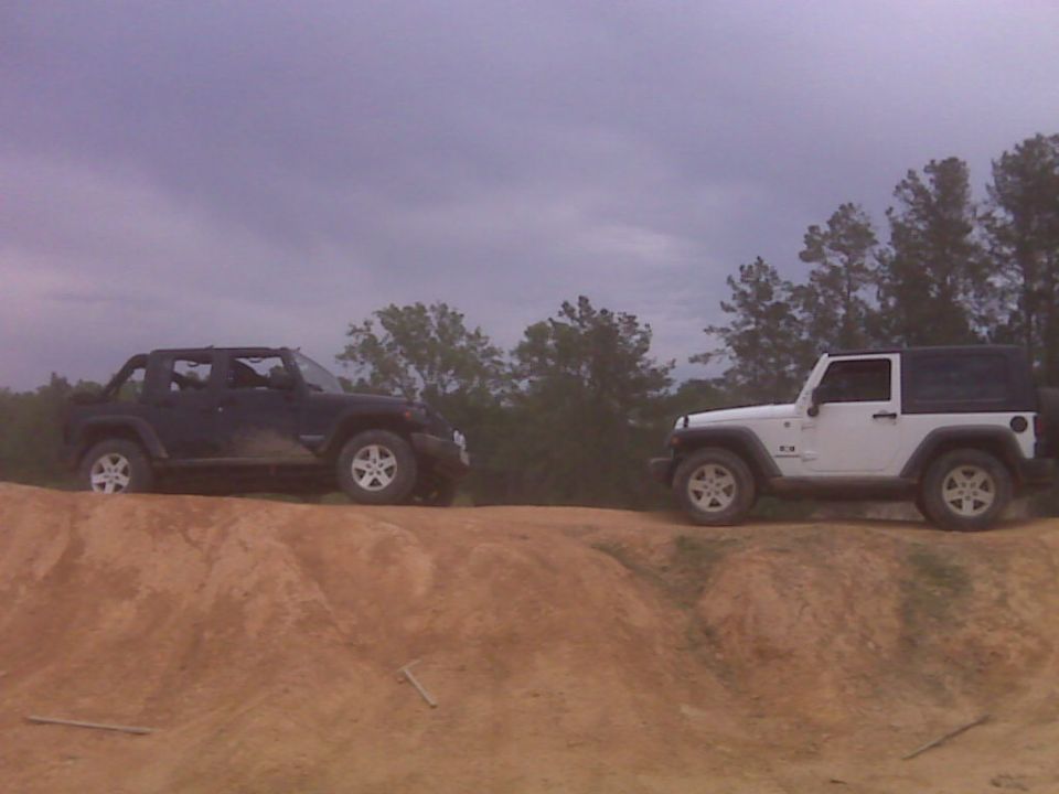 Two Jeep Wranglers parked on a dirt mound, one black and one white