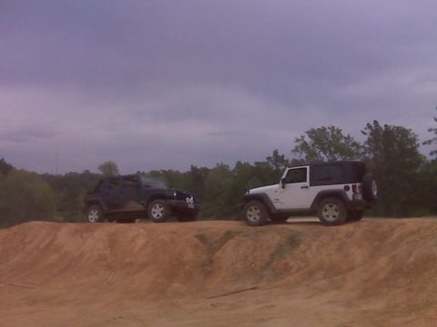 2008 Jeep Wrangler - Two Jeep Wranglers are parked on a dirt mound under a cloudy sky.