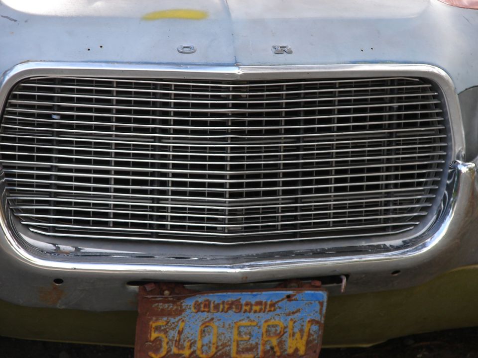 Egg-crate grille of weathered Ford with rusty blue California license plate