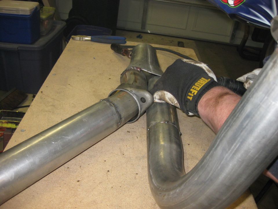 Gloved hand fitting notched bare steel tubing to a welded joint on a garage workbench