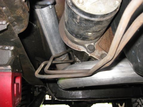 1979 Ford Bronco - Underbody shot looking up at a truck's transfer case and driveshaft, with bare-steel exhaust tubing routed past a bolted crossmember and a…