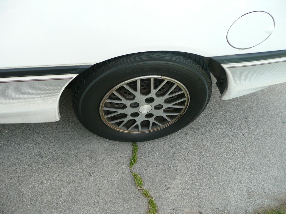 White car's rear wheel and fender with a gas cap door visible