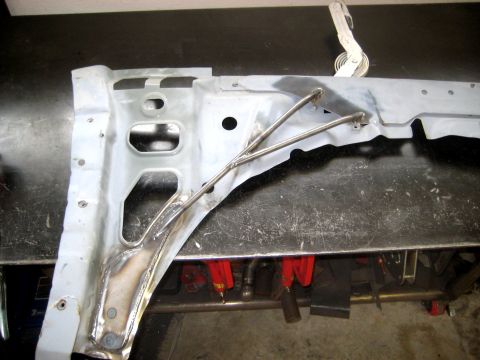 1996 Ford Bronco - A white radiator support / inner fender panel laid on a steel welding table with two bent steel tubes tacked and welded across it as a rein…